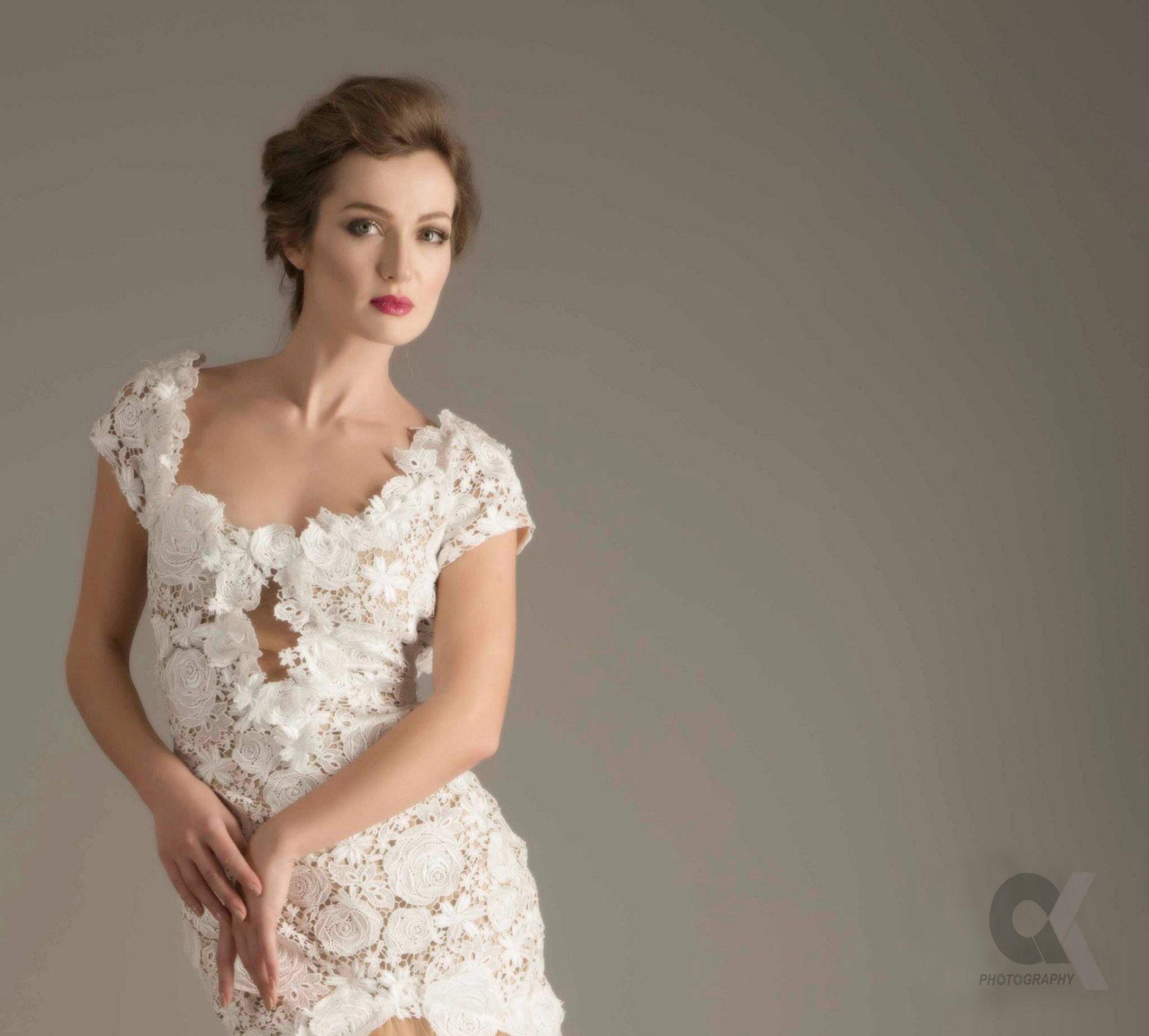 Studio portrait of a model in an intricate white lace gown.