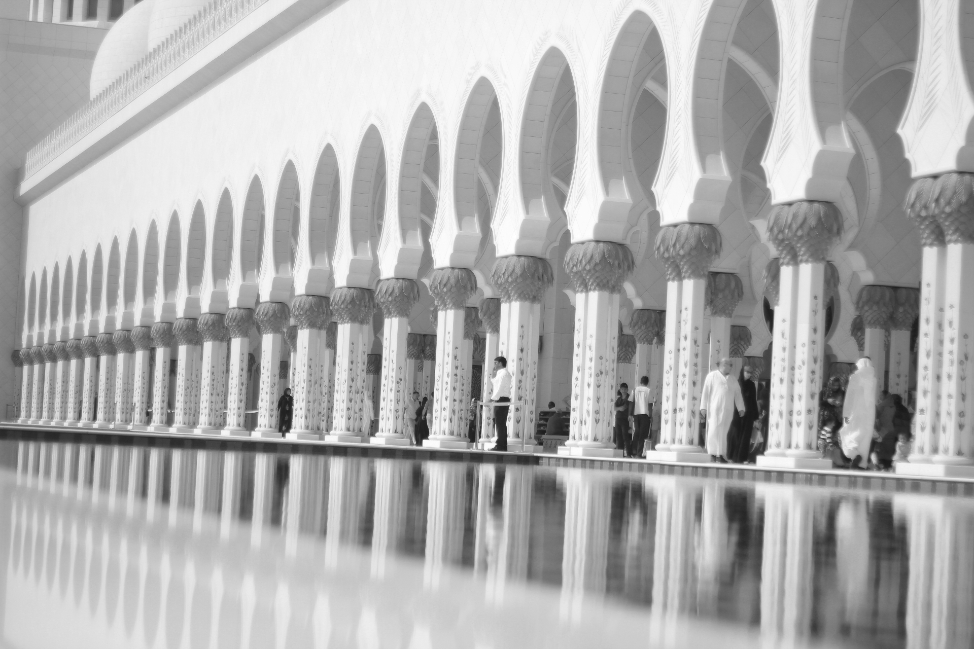 A row of ornate white arches reflected in a still pool at a grand mosque.